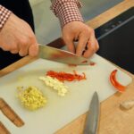 Close-up of hands chopping garlic and chili on a cutting board in a kitchen setting.