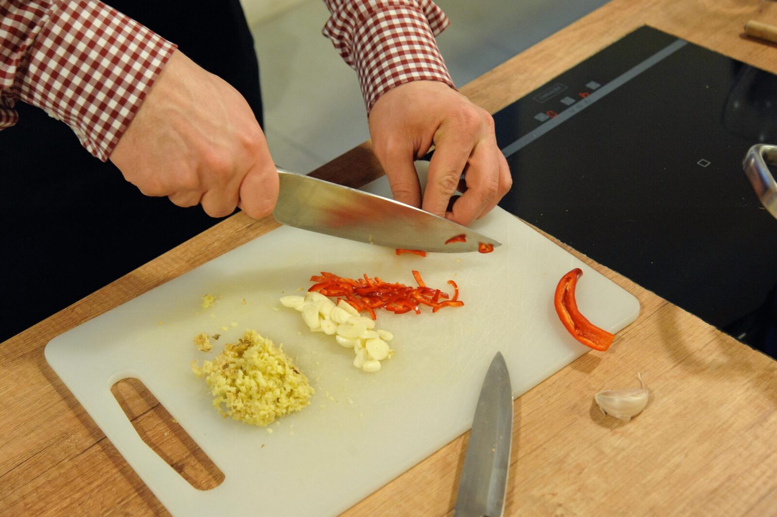 Close-up of hands chopping garlic and chili on a cutting board in a kitchen setting.