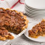 Mouthwatering pecan pie with a slice served on a white plate. Perfect for desserts or southern cuisine enthusiasts.