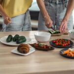 Two people preparing a healthy vegetarian meal with fresh vegetables and snacks on a wooden table.