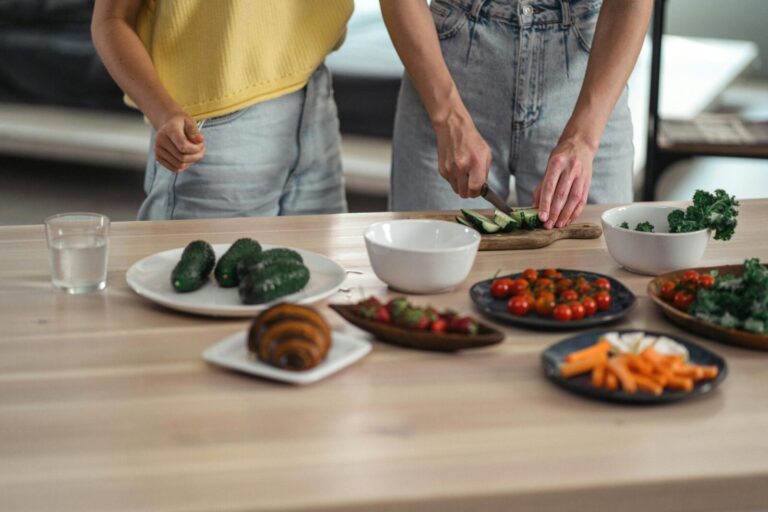 Two people preparing a healthy vegetarian meal with fresh vegetables and snacks on a wooden table.