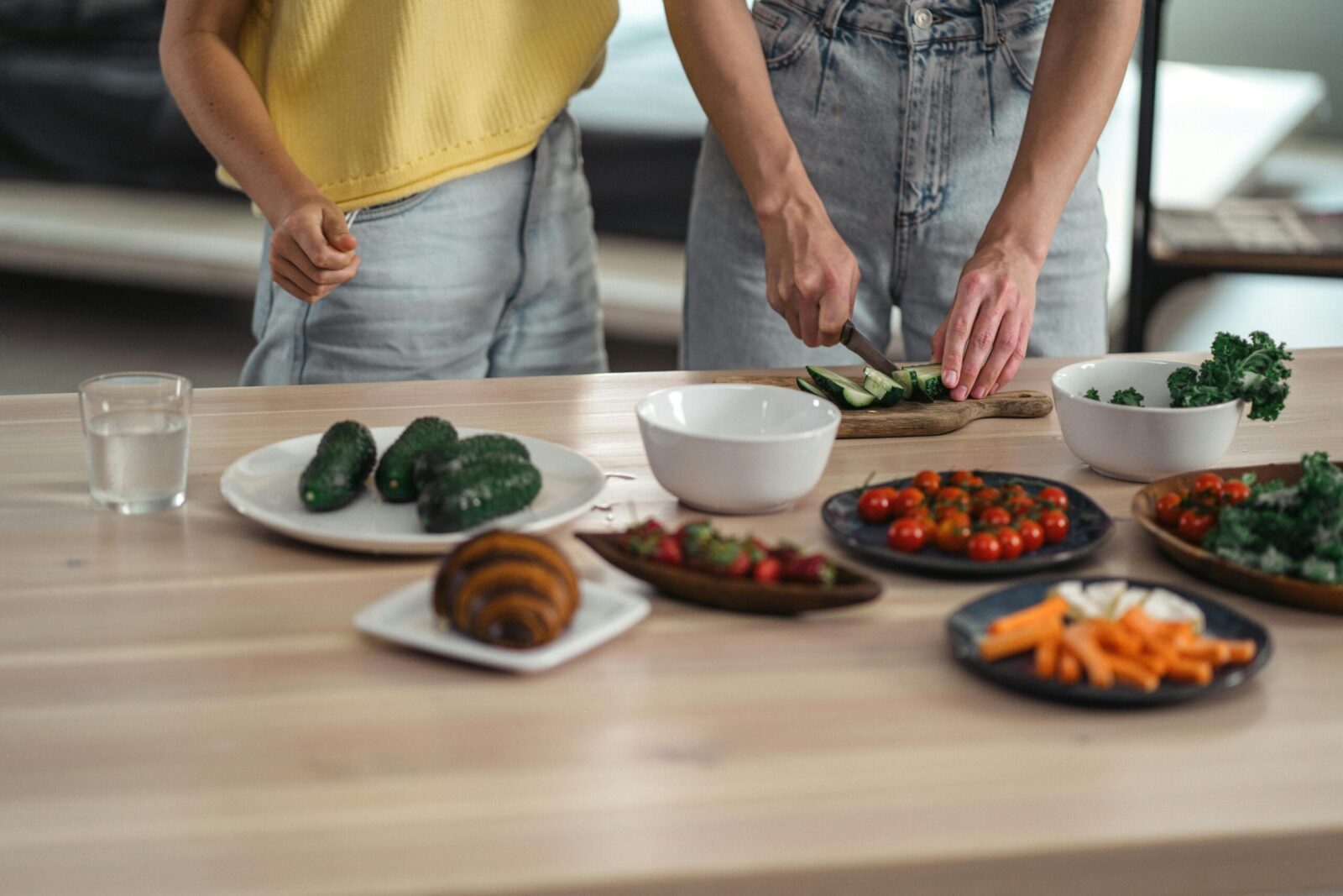 Two people preparing a healthy vegetarian meal with fresh vegetables and snacks on a wooden table.